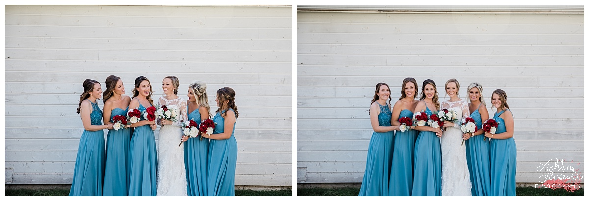 bridesmaids in blue summer dresses and red bouquets standing in front of a white brick wall