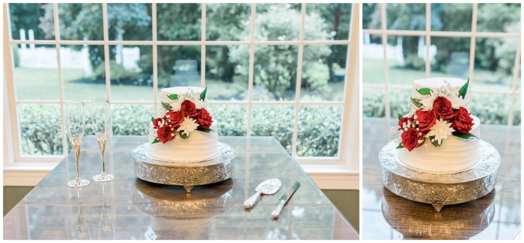 wedding cake with white buttercream, two tiers and red florals sitting on a silver cake stand with two glasses of champagne next to it for a Christopher Place military elopement