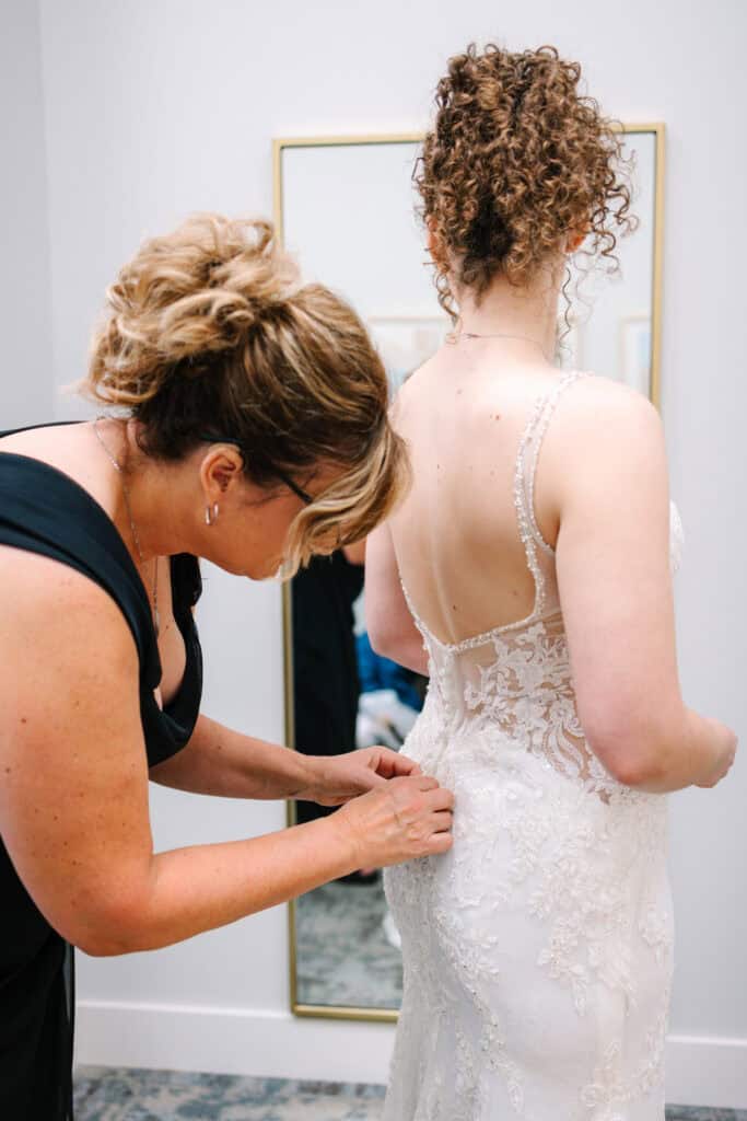 Olivia + Andrew Wedding Bridesmaid fastening the back of the bride's lace wedding dress