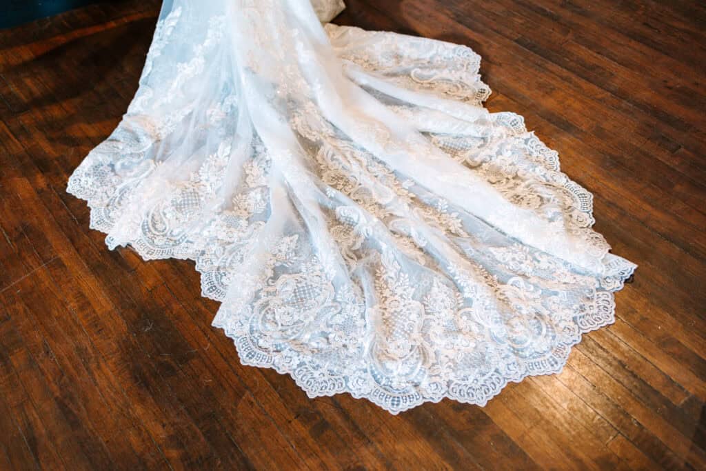 Olivia + Andrew Wedding Lace train of the bride's wedding dress spread across a wood floor