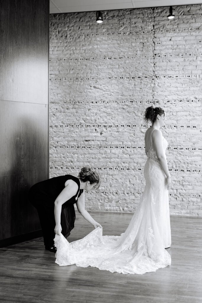 Olivia + Andrew Wedding Black and white portrait of the bride in her gown beside an exposed brick wall