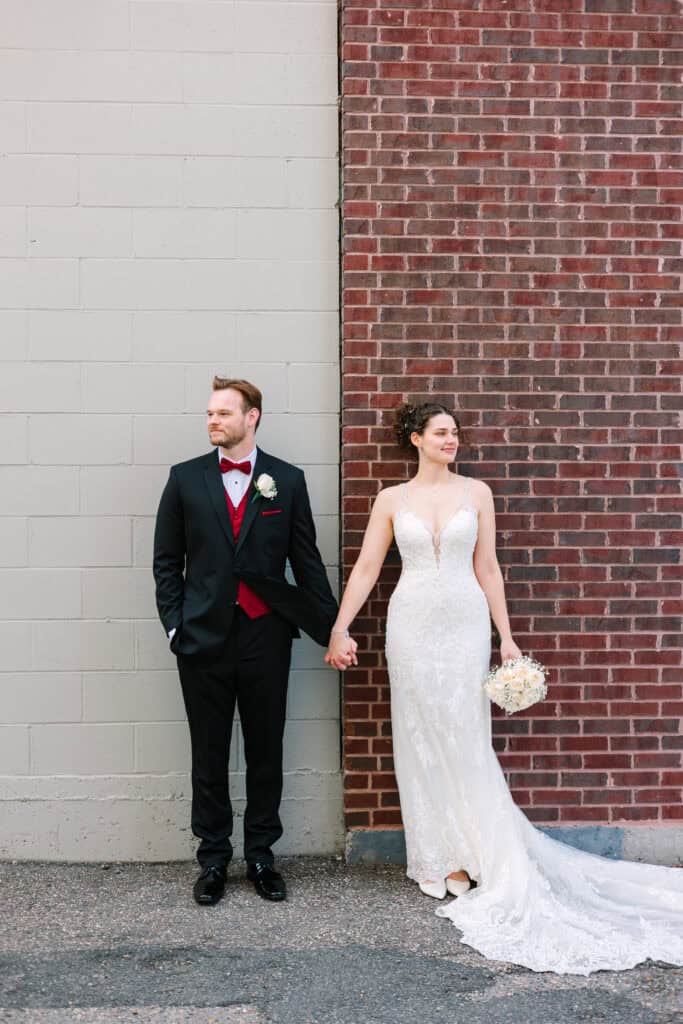 Olivia + Andrew Wedding Bride and groom holding hands during portraits beside a brick wall