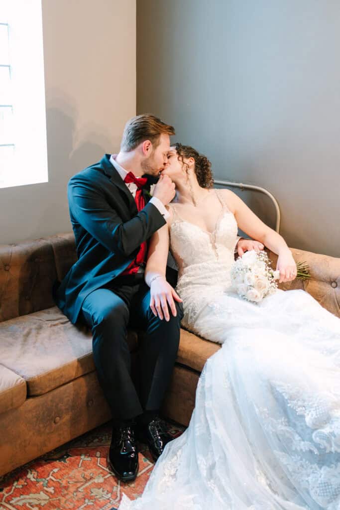 Olivia + Andrew Wedding Newlyweds kissing while seated together on a couch