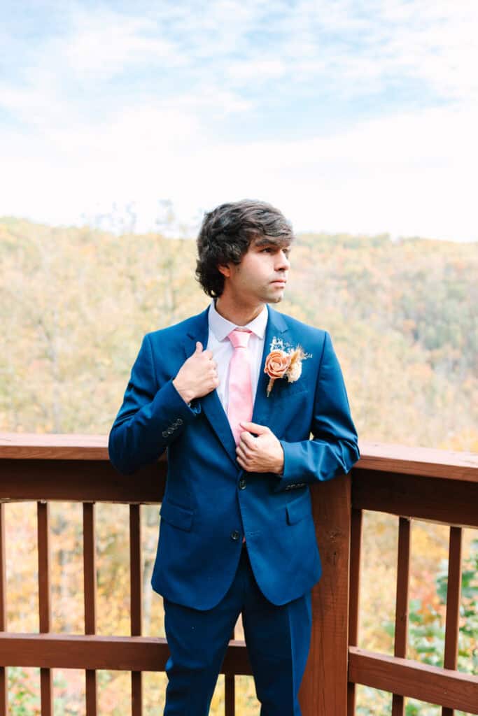 Groom adjusting his pink tie on a cabin deck overlooking the mountains