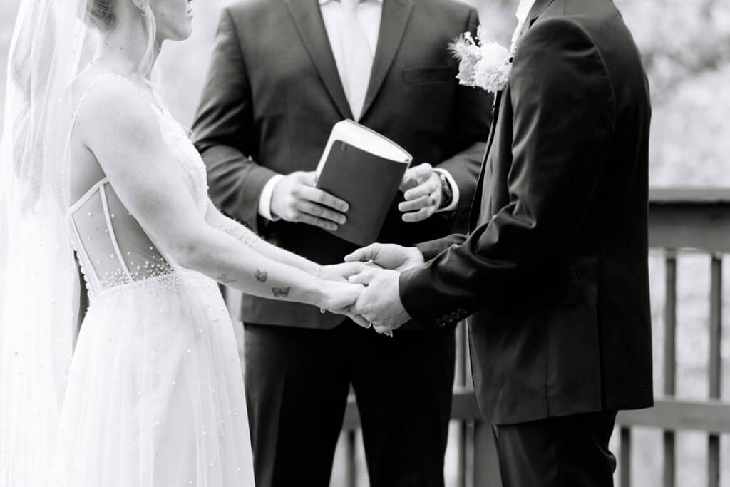 Black and white close-up of the couple holding hands during the ceremony