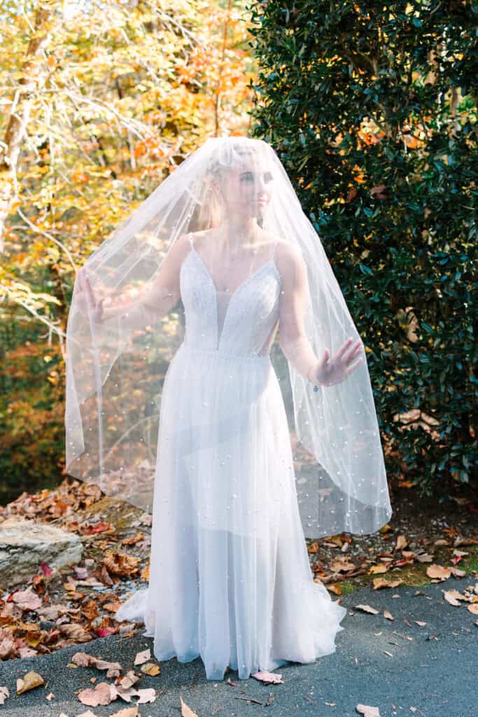 Bride showing her long veil and open-back wedding dress on a fall path