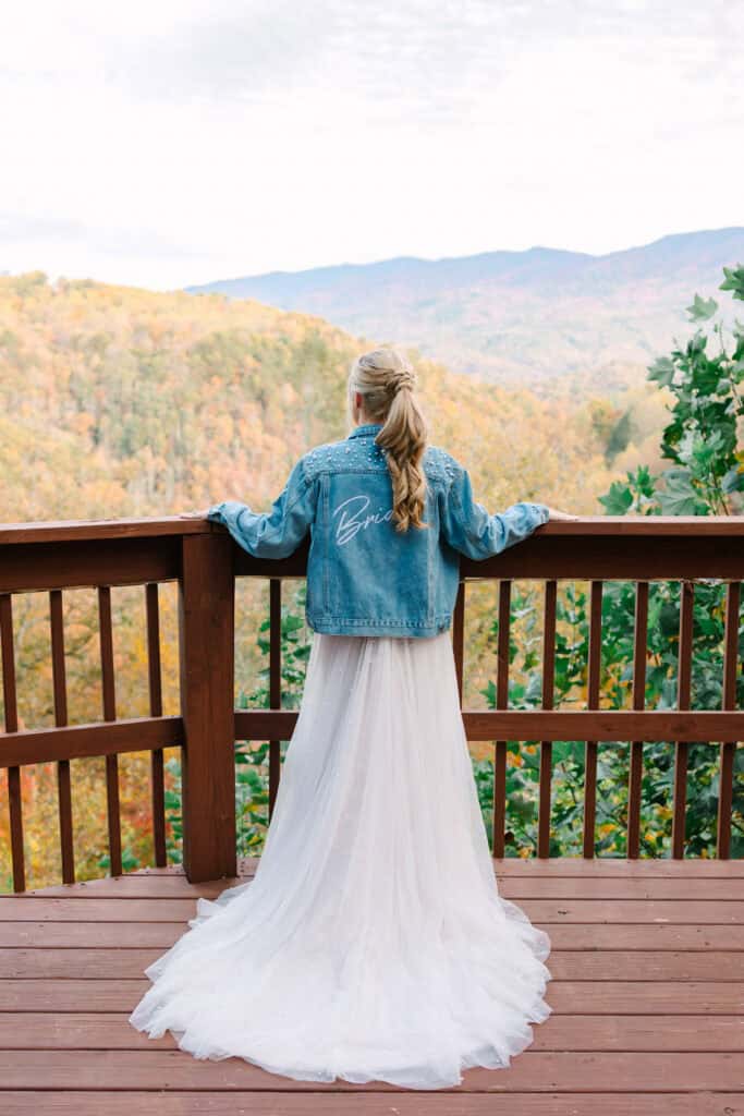 Bride in a denim jacket looking over the Smoky Mountains from a cabin deck