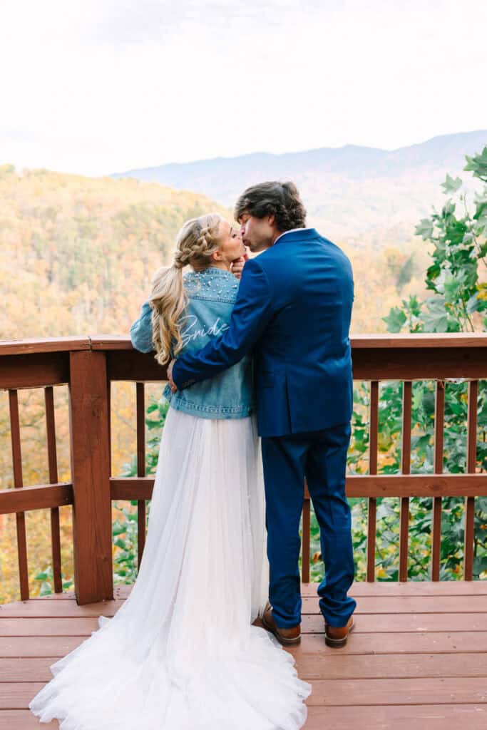 Groom hugging the bride from behind on a cabin deck with mountain views
