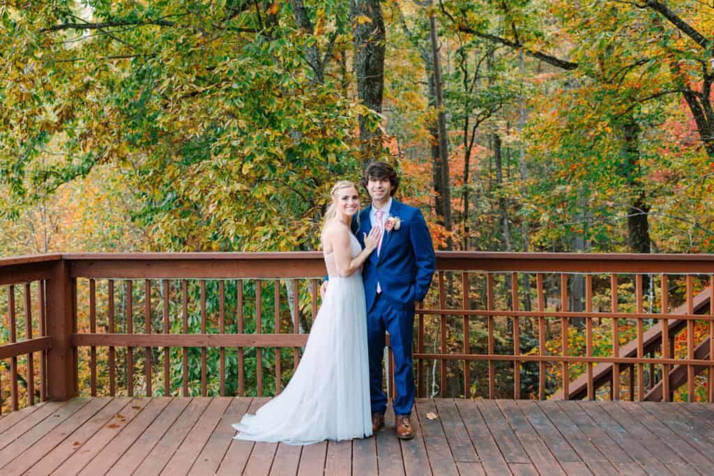 Bride and groom standing together on a cabin deck surrounded by fall color