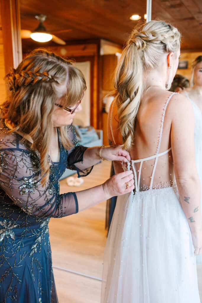 Bridesmaid fastening the back of the bride's wedding dress