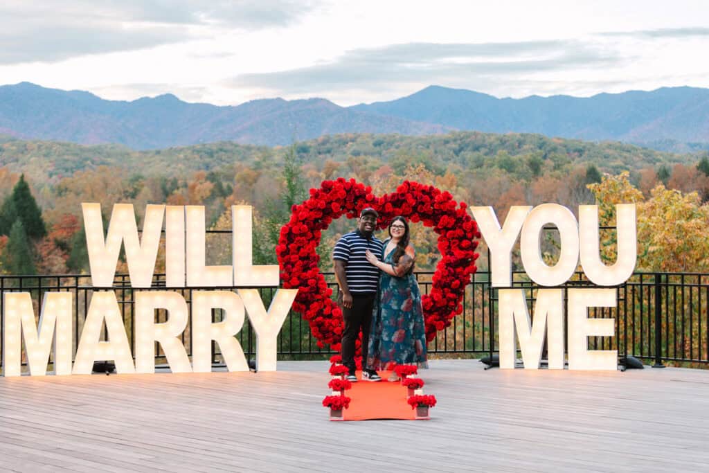 Bobby + Alyssa Proposal Newly engaged couple embracing inside a rose heart with mountain views