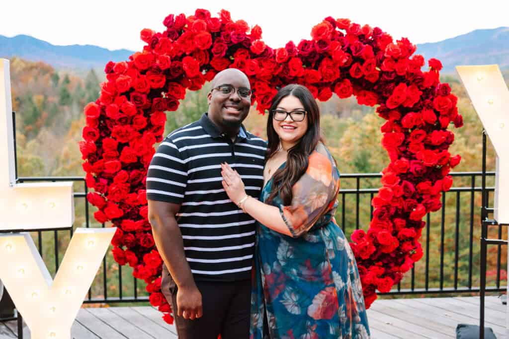 Bobby + Alyssa Proposal Engaged couple smiling together beneath a red rose heart
