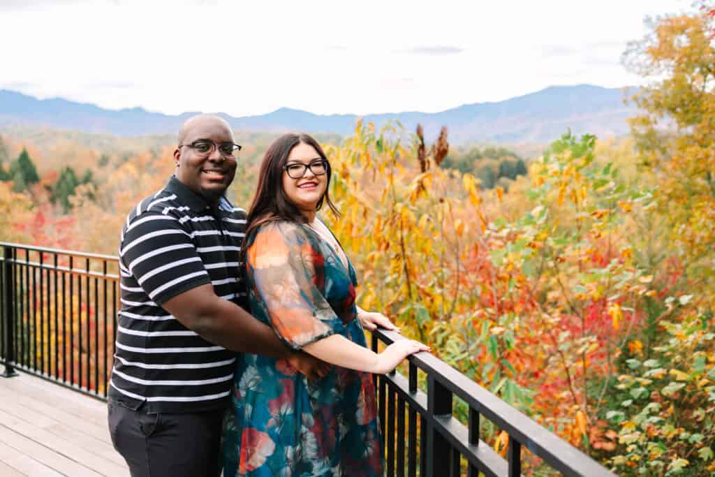 Bobby + Alyssa Proposal Newly engaged couple standing at a railing with colorful fall mountains behind them