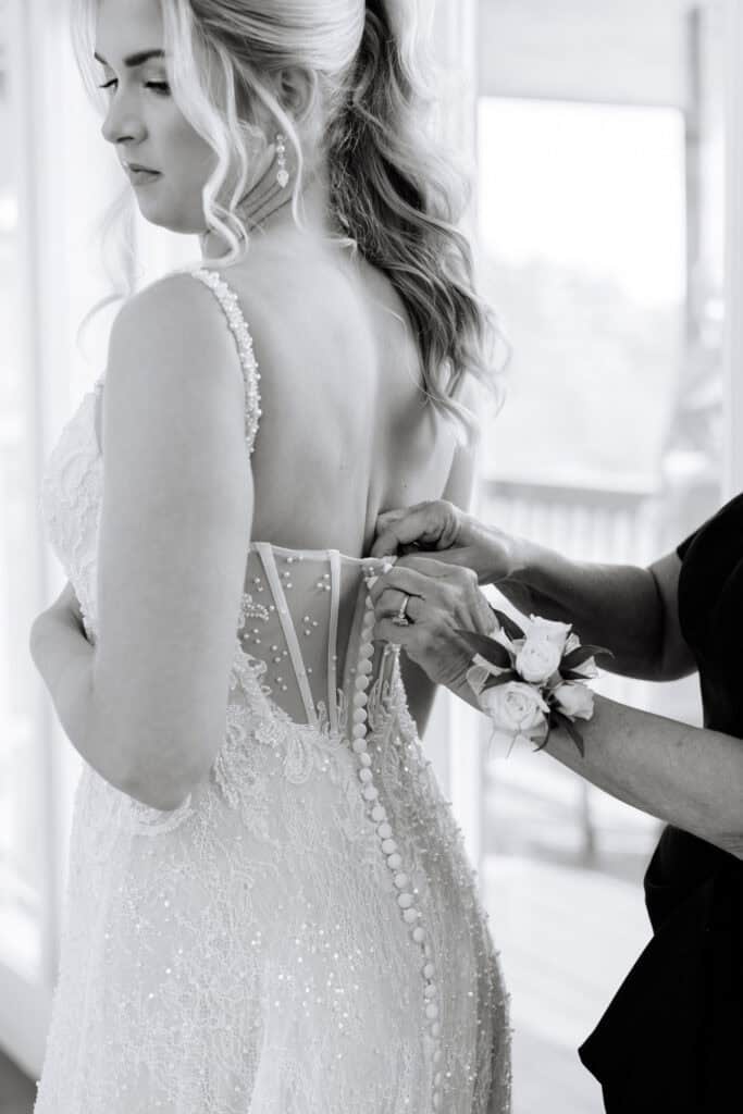 Lauren + Connor Wedding Black-and-white close-up of hands fastening the bride's gown