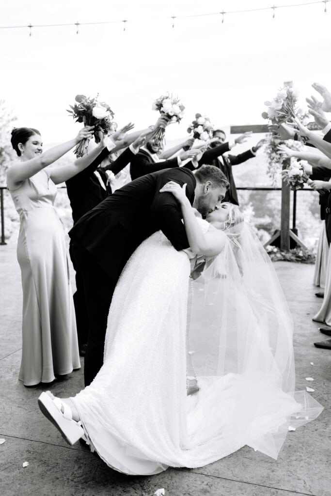Lauren + Connor Wedding Groom poses in a navy tuxedo among the trees