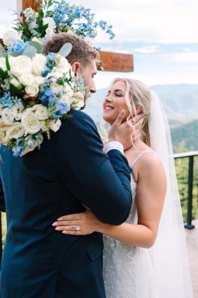 Lauren + Connor Wedding Bride hugs the groom beside the ceremony cross and blue flowers