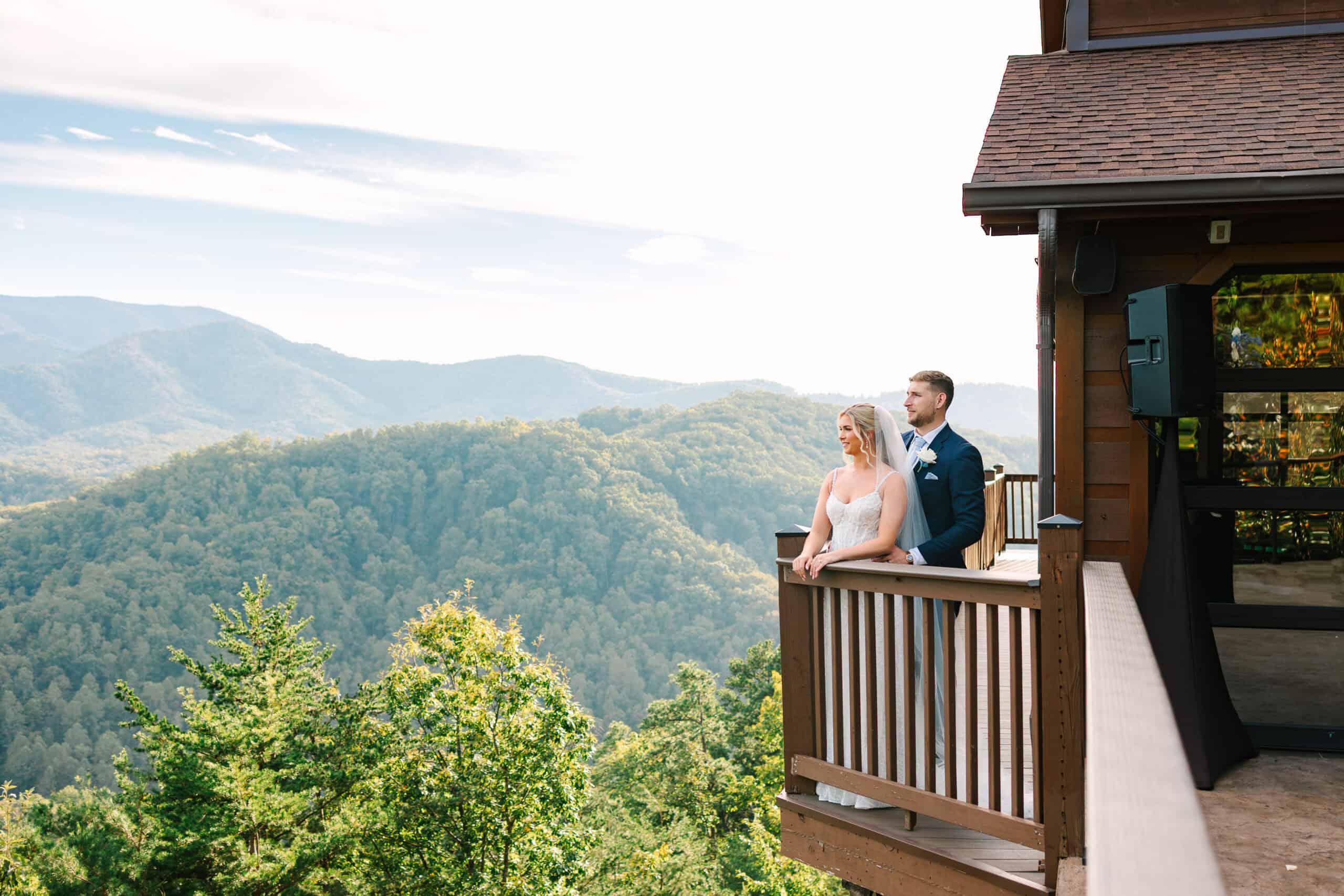 Wide portrait of the couple on a cabin balcony with mountain ridges behind them