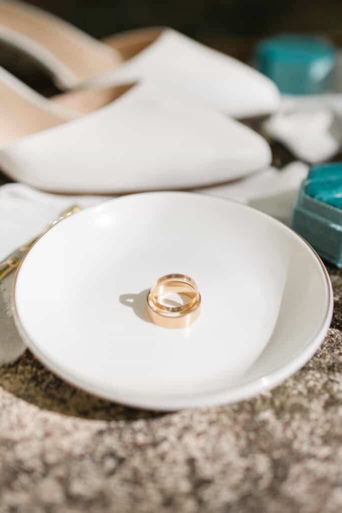 Thaís + Nick Wedding Wedding rings resting in a small white dish on stone