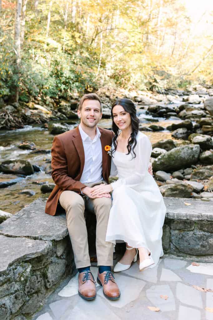 Thaís + Nick Wedding Newlyweds sitting on a stone wall beside the Little River