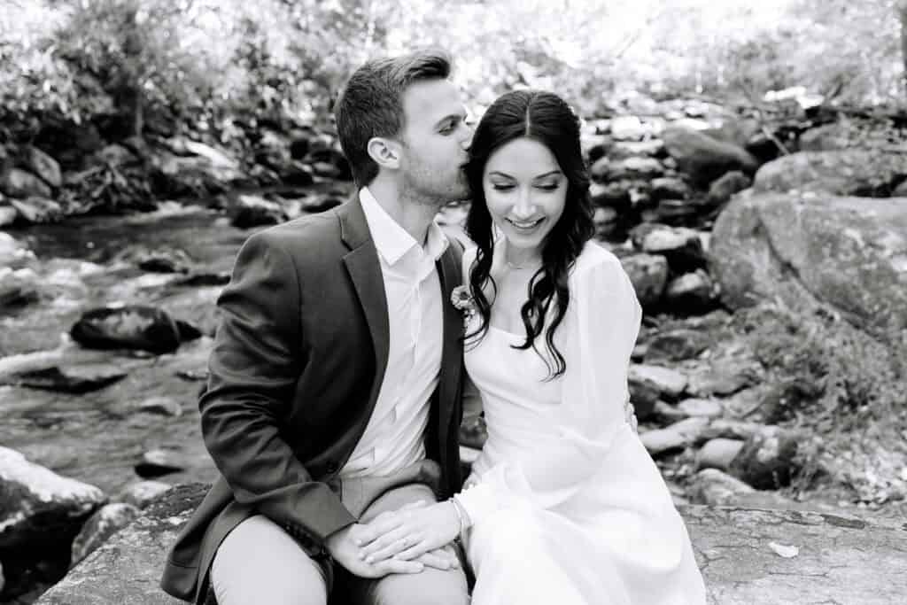 Thaís + Nick Wedding Black and white photo of the couple sitting by the river rocks
