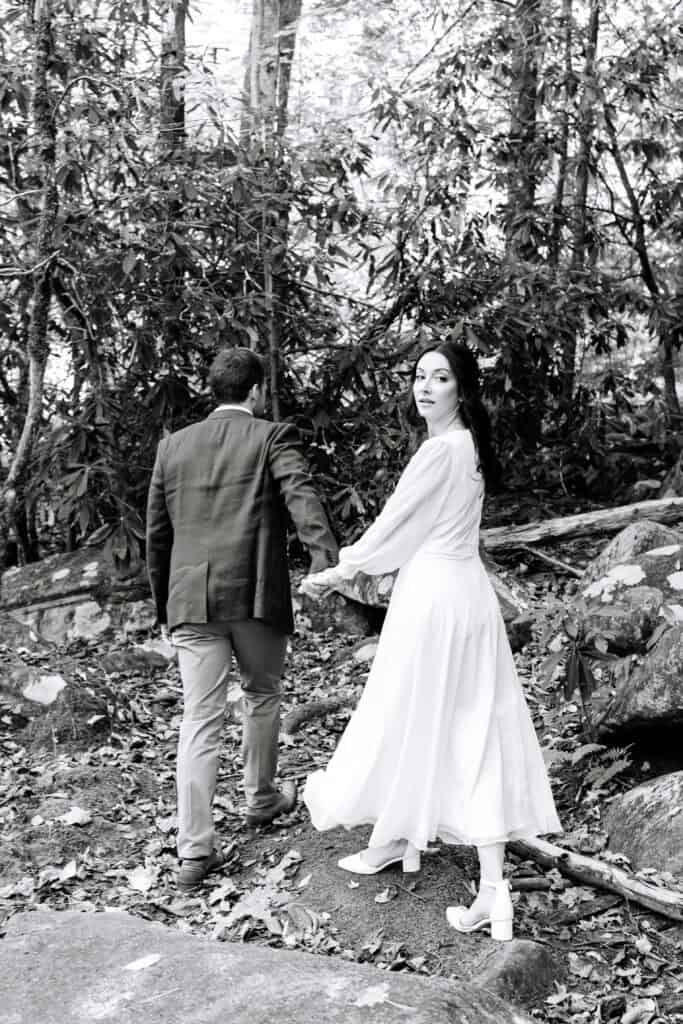 Thaís + Nick Wedding Black and white photo of the bride leading the groom through the trees