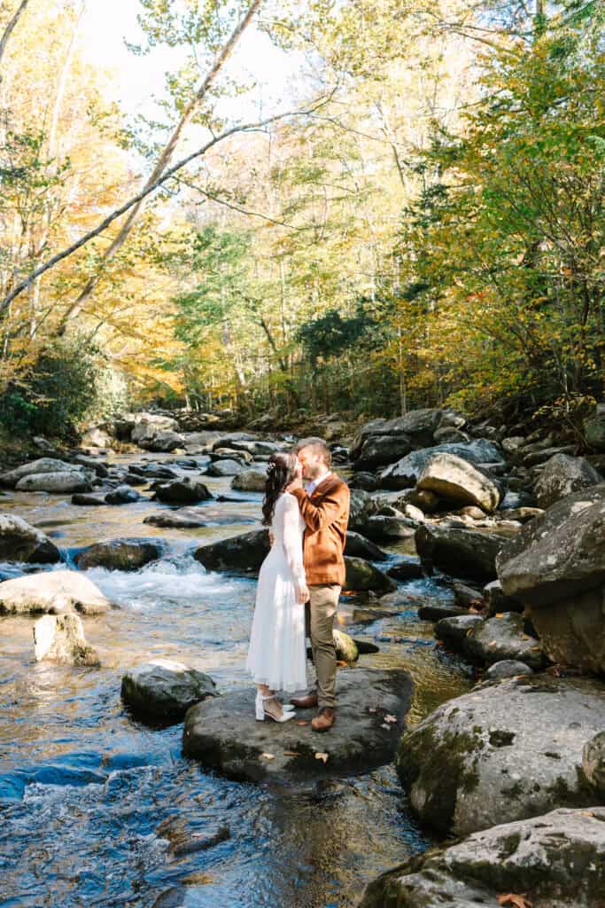 Thaís + Nick Wedding Couple standing on rocks in the Little River with golden leaves above