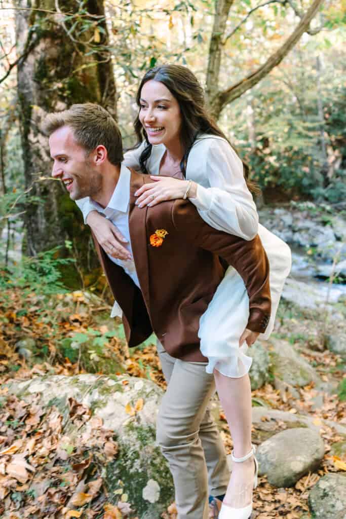 Thaís + Nick Wedding Groom giving the bride a piggyback ride through the woods