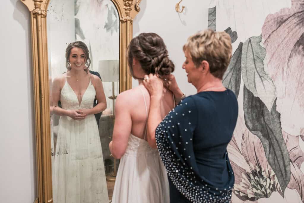 Sarah + Jake Wedding Mom buttoning the back of the bride’s gown