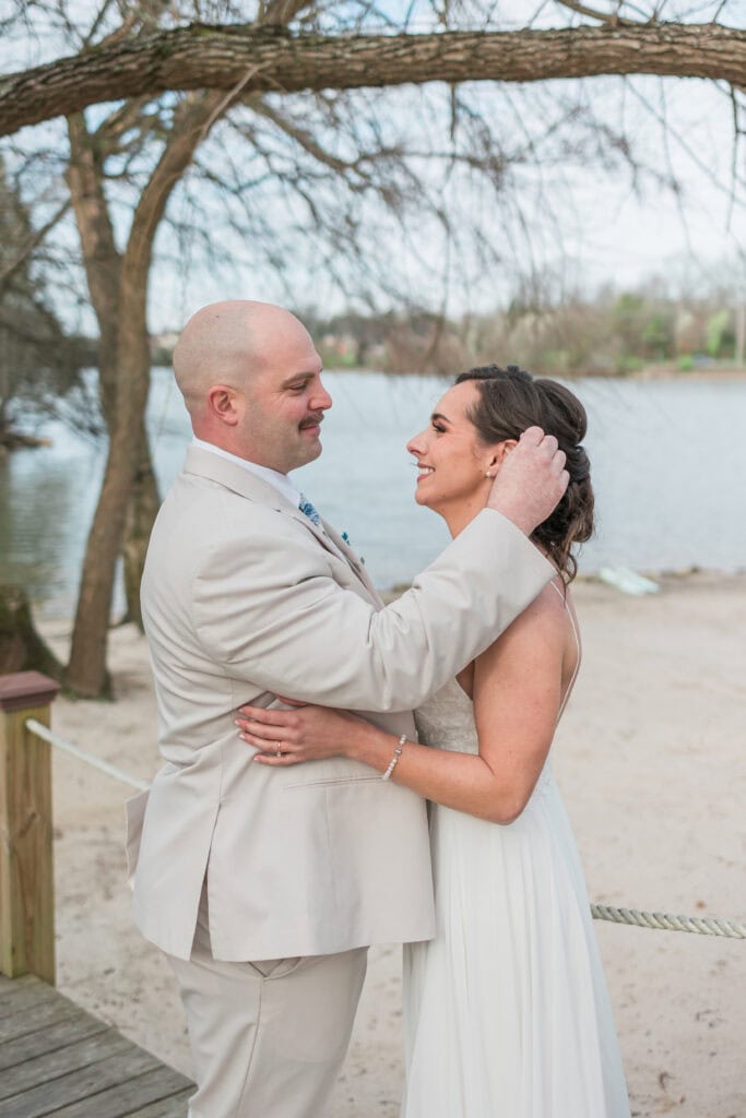Sarah + Jake Wedding Groom holding the bride’s face by the lake
